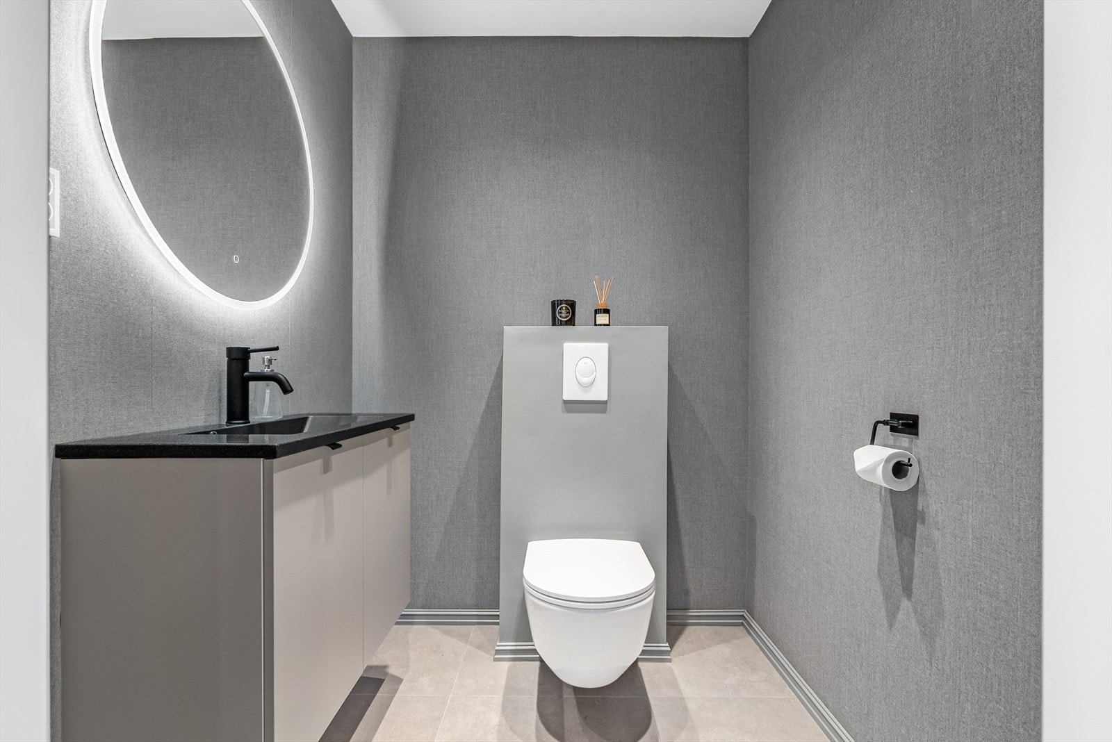 I hovedetasjen ved kjøkkenet er det et toalettrom med fliser på gulv og tapetserte vegger. Rommet har vegghengt toalett, servant med underskap og speil med belysning. Praktisk for gjester. Galleribilde