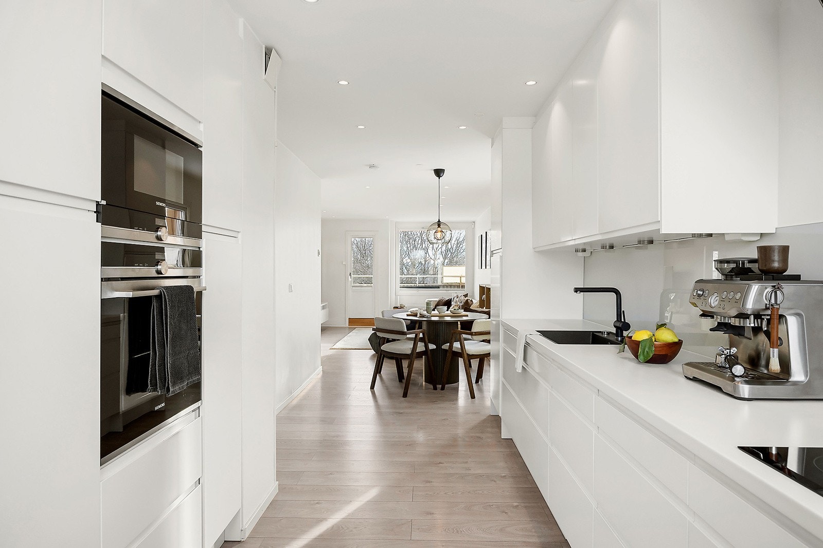 Kjøkkeninnredning med slette fabrikklakkerte fronter og integrert stekeovn, koketopp, mikroovn, fryser og oppvaskmaskin. Galleribilde