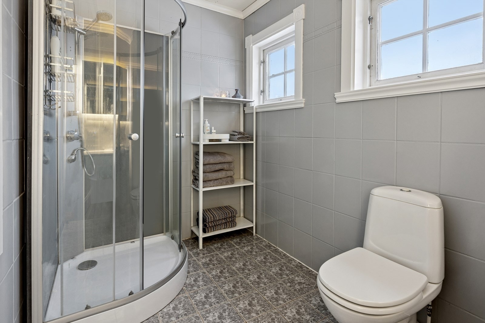 Badet er innredet med et gulvstående toalett, dusjkabinett og et servantskap med nedfelt servant. Galleribilde