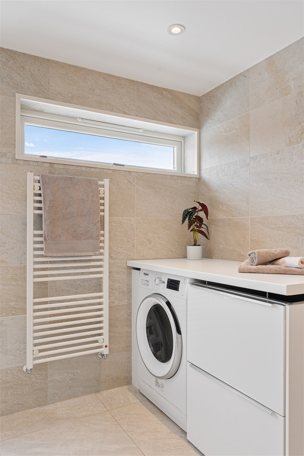 Opplegg for vaskemaskin med benkeløsning i et hjørne av badet. Her er også håndklevarmer. Galleribilde