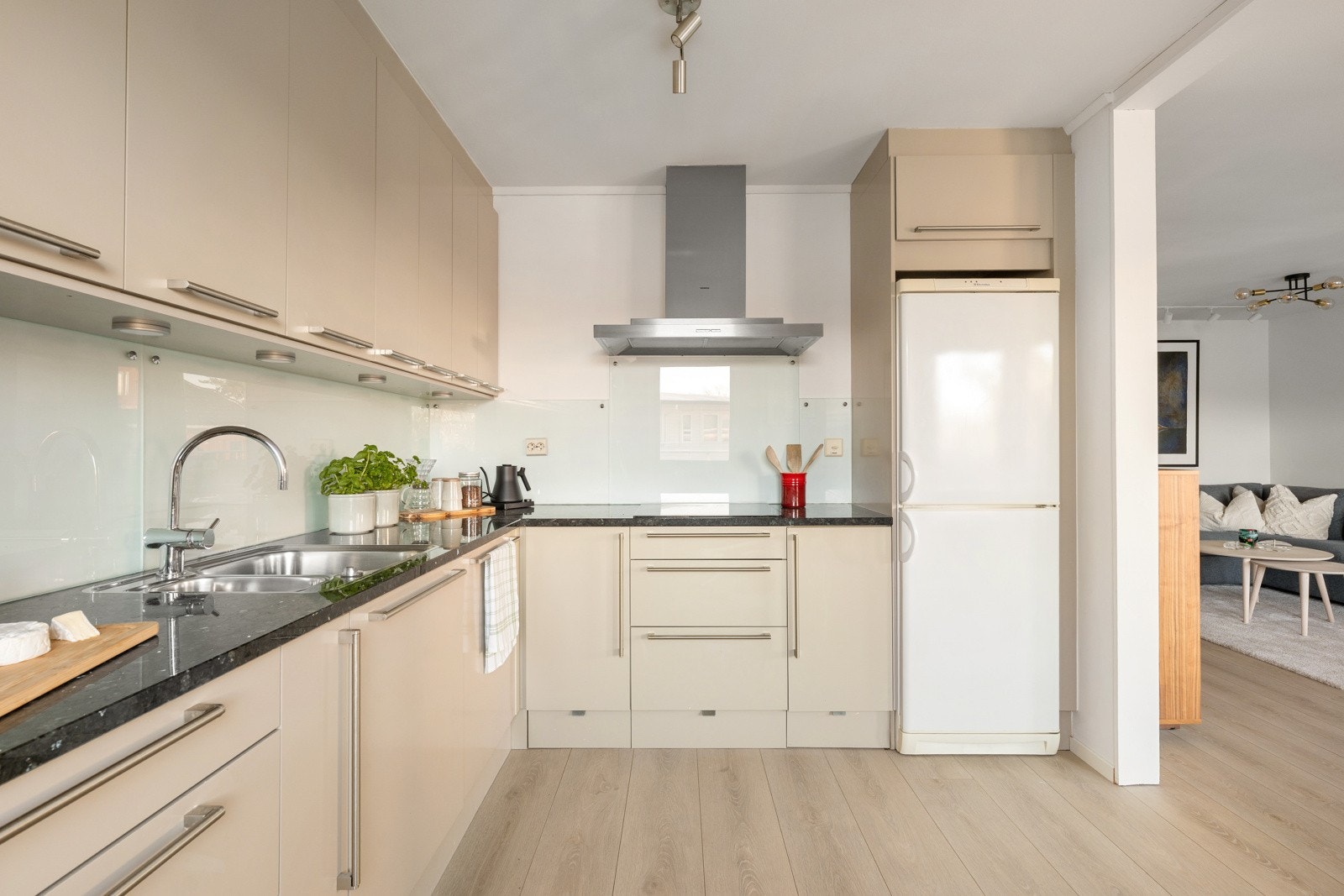 Integrerte hvitevarer og frittstående kjøleskap gir et helhetlig uttrykk, og den åpne plasseringen mot stuen gjør kjøkkenet til en naturlig del av oppholdsrommet. Galleribilde