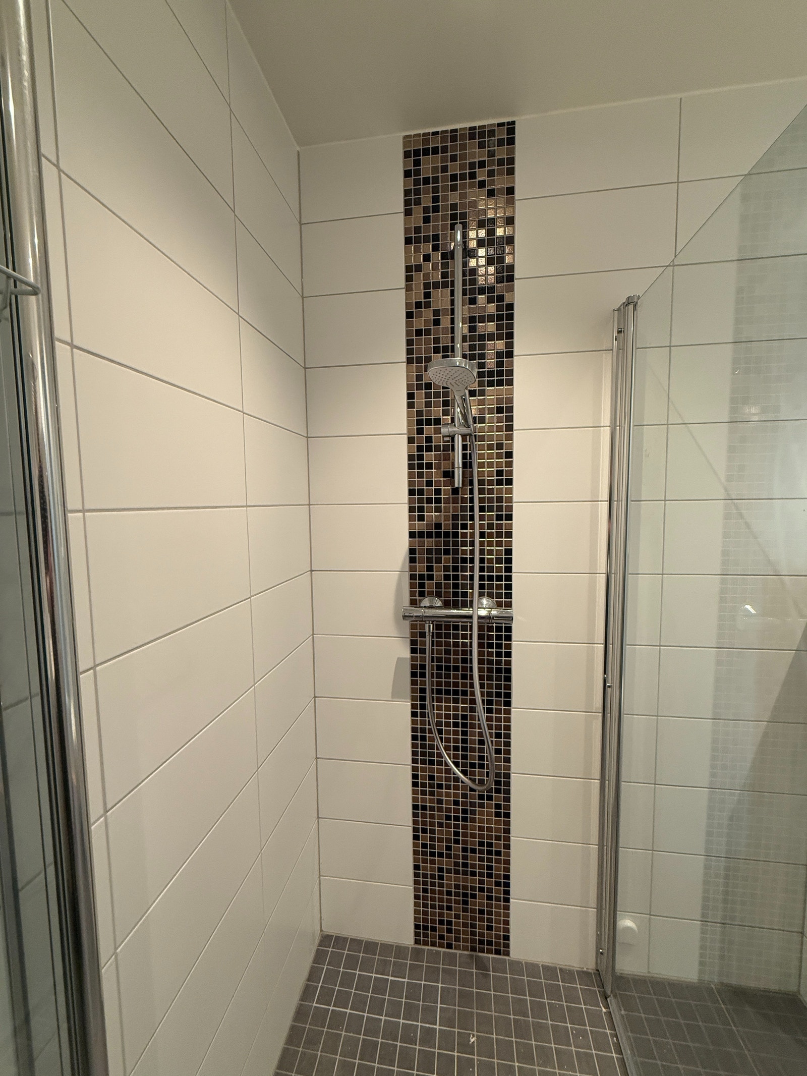 Delikat, flislagt bad med dusjhjørne på 90x90cm og moderne mosaikkdetaljer. Tidløst uttrykk og enkelt vedlikehold. Galleribilde