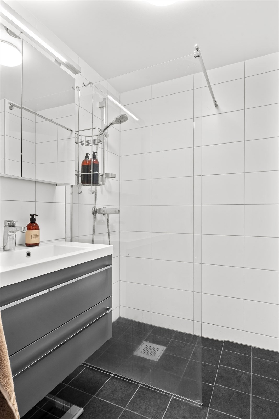 Innredning beståenen av vegghengt klosett, to servanter, hvorav en av de har innredning og dusjhjørne med glassvegg. Det er mekanisk avtrekk. Galleribilde