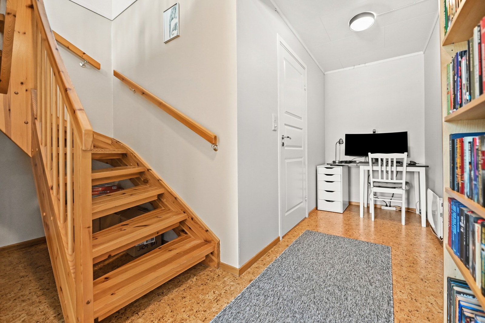 Kontorområde med skrivebord ved siden av trapp, vegger malt i lys farge og gulv med korkbelegg. Galleribilde