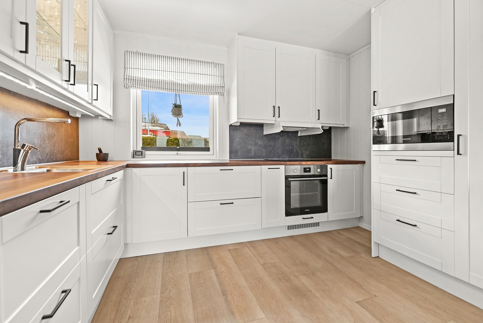 Lyst kjøkken med moderne hvitevarer, godt med skapplass og vindu som gir naturlig lys. Galleribilde