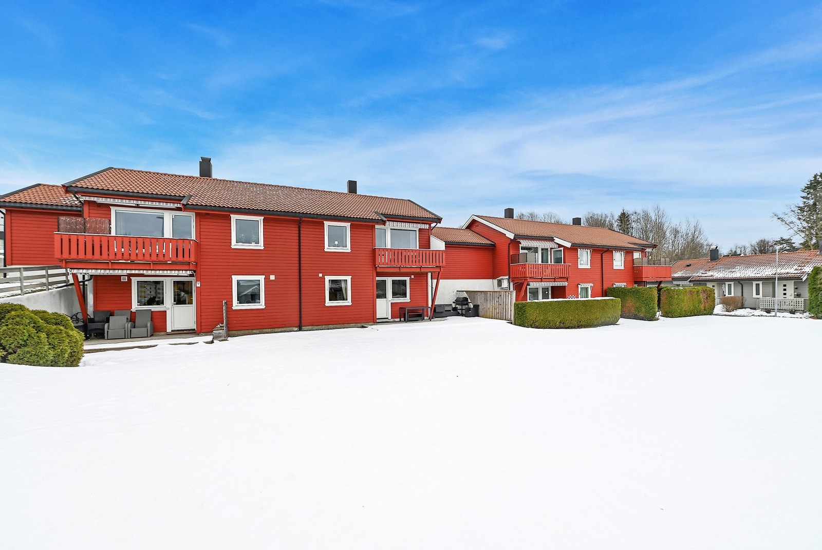 Tomannsbolig med røde fasader, balkonger og snødekt uteområde. Galleribilde