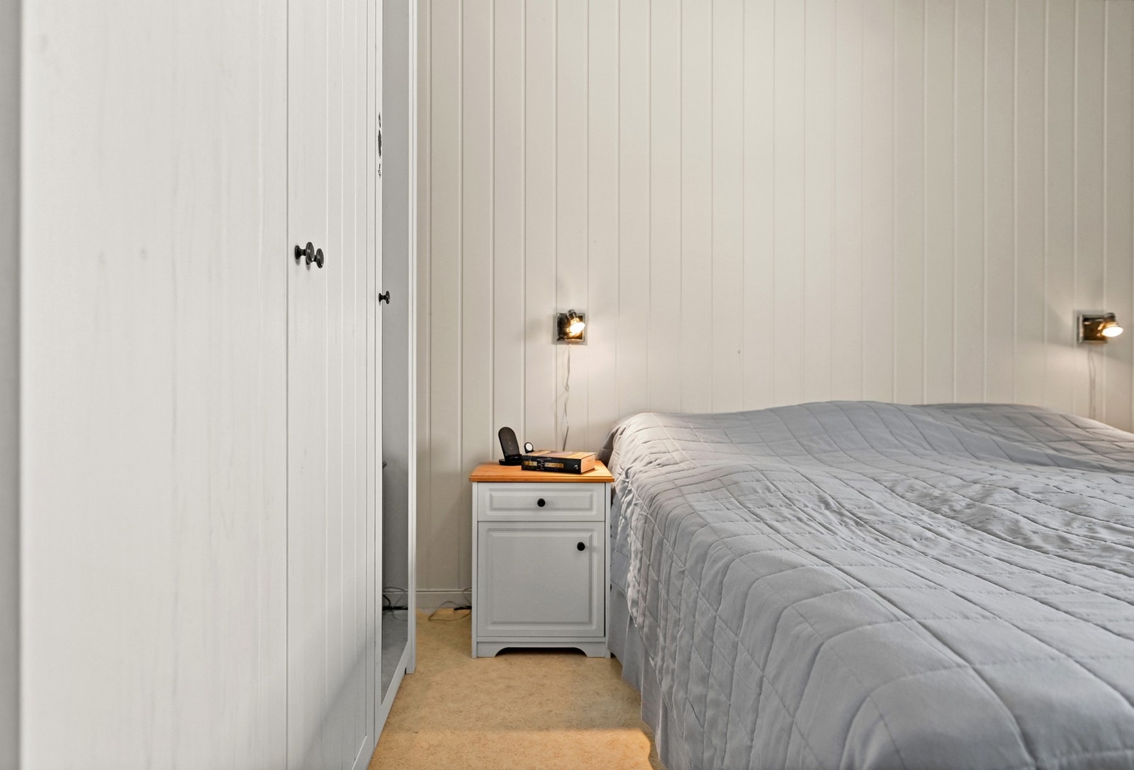 Soverom med lysmalte panelvegger, innebygd garderobe og nattbord ved siden av sengen. Galleribilde