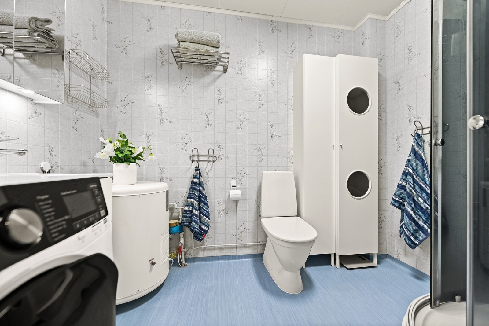 Bad med lyse fliser, dusjkabinett, toalett, varmtvannsbereder og vaskemaskin. Galleribilde