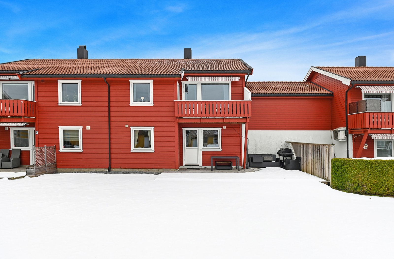 Tomannsbolig med rødmalt fasade, balkong og uteplass, beliggende i et rolig område. Galleribilde