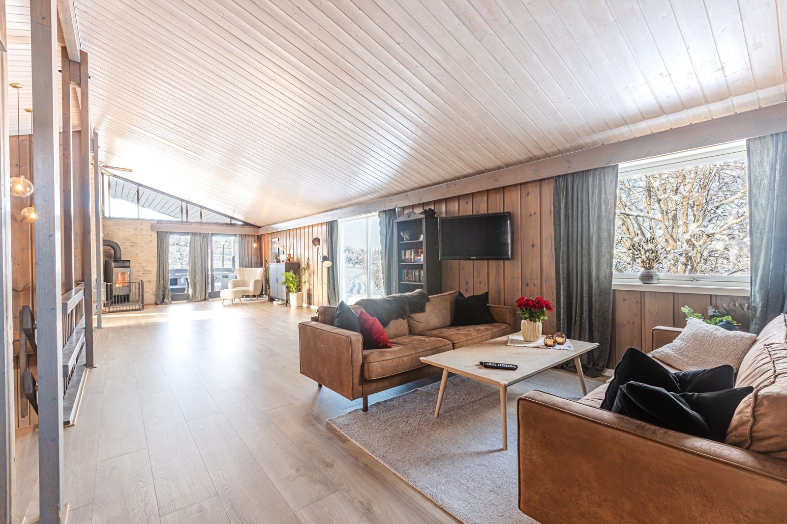 Store vindusflater gir godt lysinnslipp i stuen, som har parkettgulv og panelerte vegger. Vedovn med glassdør bidrar til en behagelig varme i oppholdsrommet. Galleribilde