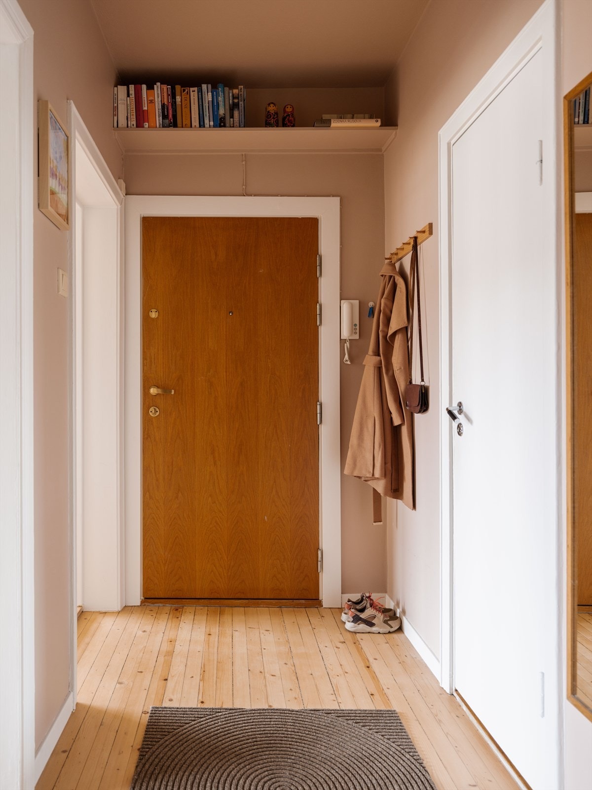 Over inngangsdøren er det også en oppbevaringshylle som utnytter takhøyden godt. Rommet gir et ryddig og funksjonelt førsteinntrykk av boligen. Galleribilde