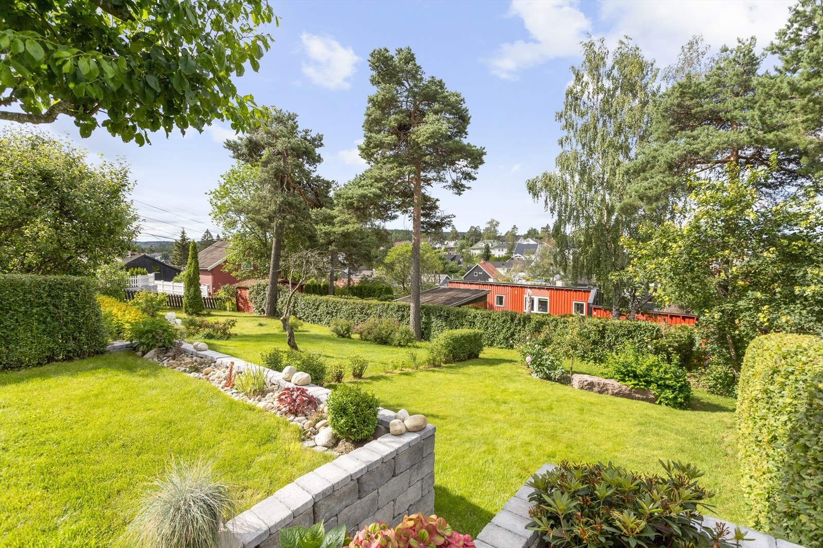 Tomten er skrå og opparbeidet med plen og beplantning, noe som gir en fin ramme rundt eiendommen. (Bildene er tatt tilbake i 2019). Galleribilde