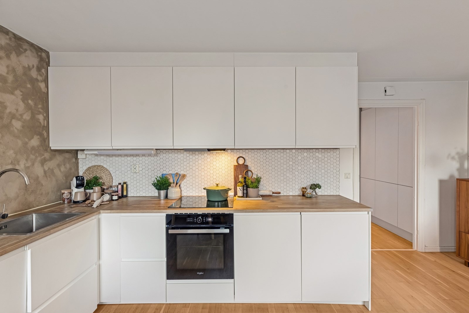 Kjøkkeninnredning med glatte folierte fronter, tre benkeplate med nedfelt rustfri kum, fliser på vegg over benk og ventilasjon via kanal/system. Galleribilde