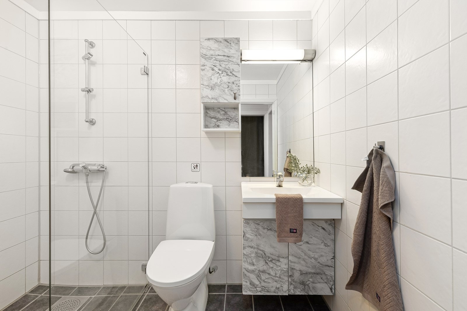 Flislagt bad med dusj, toalett og servant med servantskap. Galleribilde