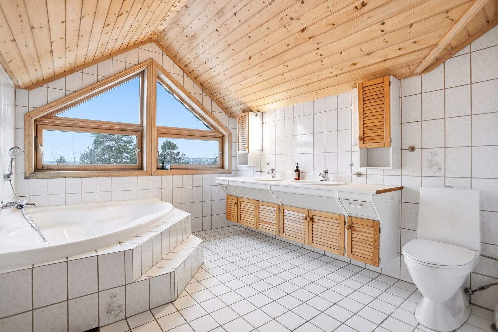 Flislagt bad som er innredet med toalett, innmurt hjørnebadekar, dusjnisje og baderomsinnredning med to servanter. Varmekabler i gulv. Galleribilde