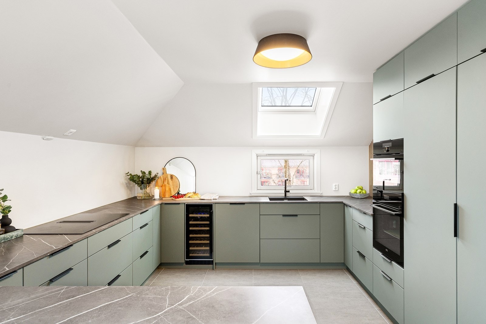 Kjøkkenet fremstår moderne og gjennomført med fronter i en dempet grønn tone som gir et eksklusivt og rolig uttrykk. Fargen harmonerer godt med de lyse overflatene og skaper en lun kontrast mot benkeplaten, samtidig som helheten oppleves tidløs. Galleribilde