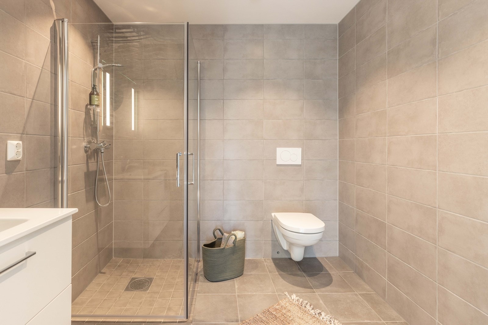 Badet er innredet med baderomsinnredning med heldekkende servant, speil med belysning, vegghengt toalett og dusjhjørne med glassdører. Galleribilde