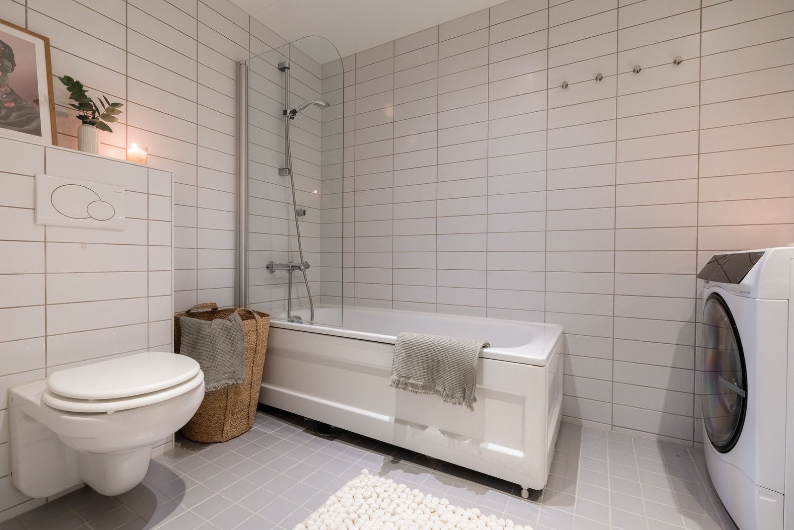 Videre er det vegghengt toalett og badekar med dusj samt glassvegg. Badet benyttes som boligens vaskerom med opplegg for vaskemaskin og plass til tørketrommel. Galleribilde