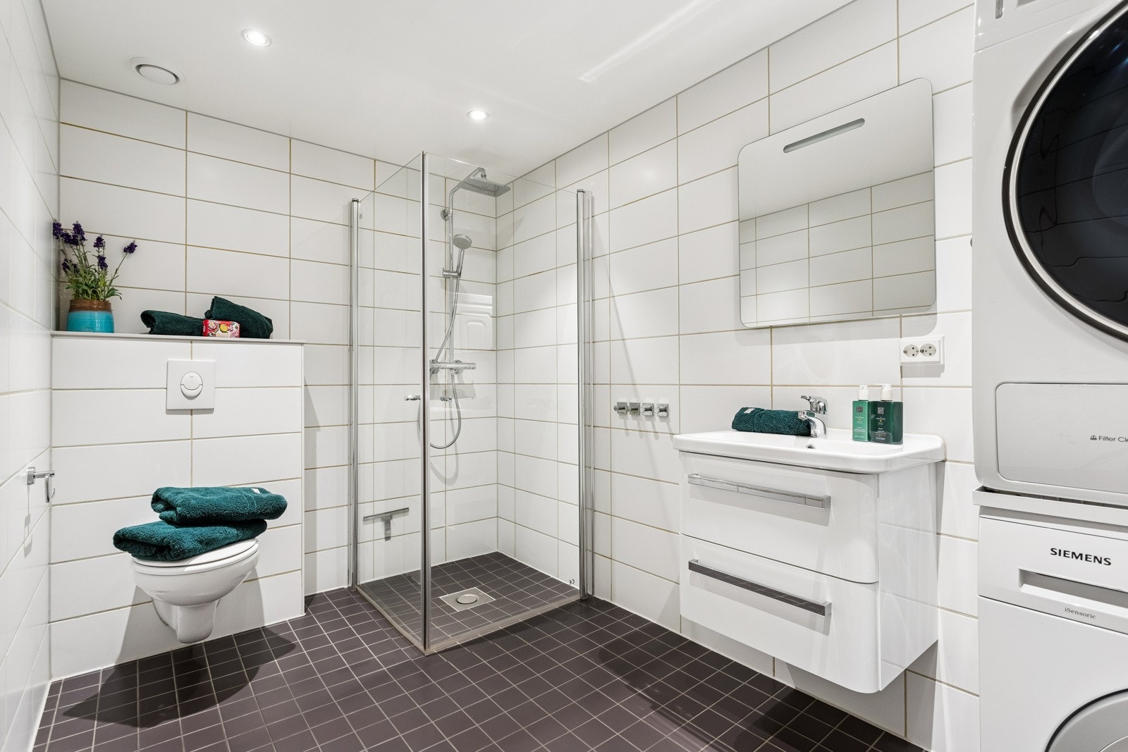 Delikat flislagt bad innredet med dusjvegger, servant med underskap og veggklosett. Opplegg for vaskemaskin. Galleribilde