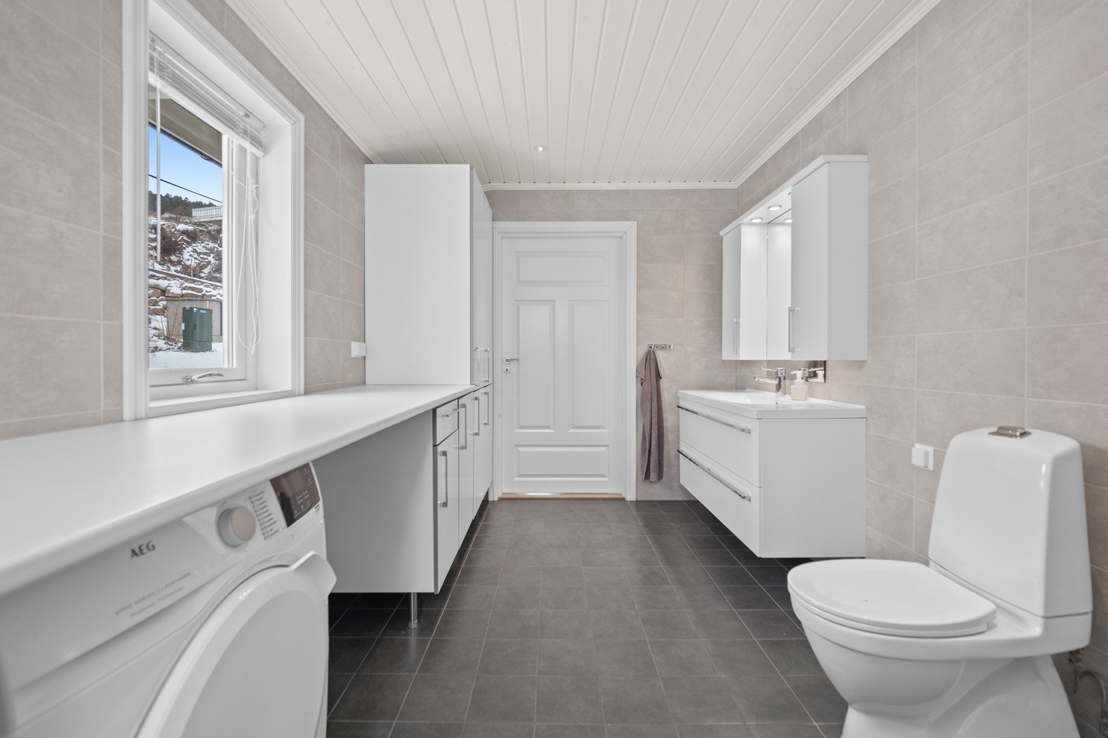 Vegghengt møblement ved speil og gulvstående innredning med slette fronter og benkeplater av laminat. Dusjhjørne med innfellbare glassdører, gulvstående toalett og opplegg for vaskemaskin. Galleribilde