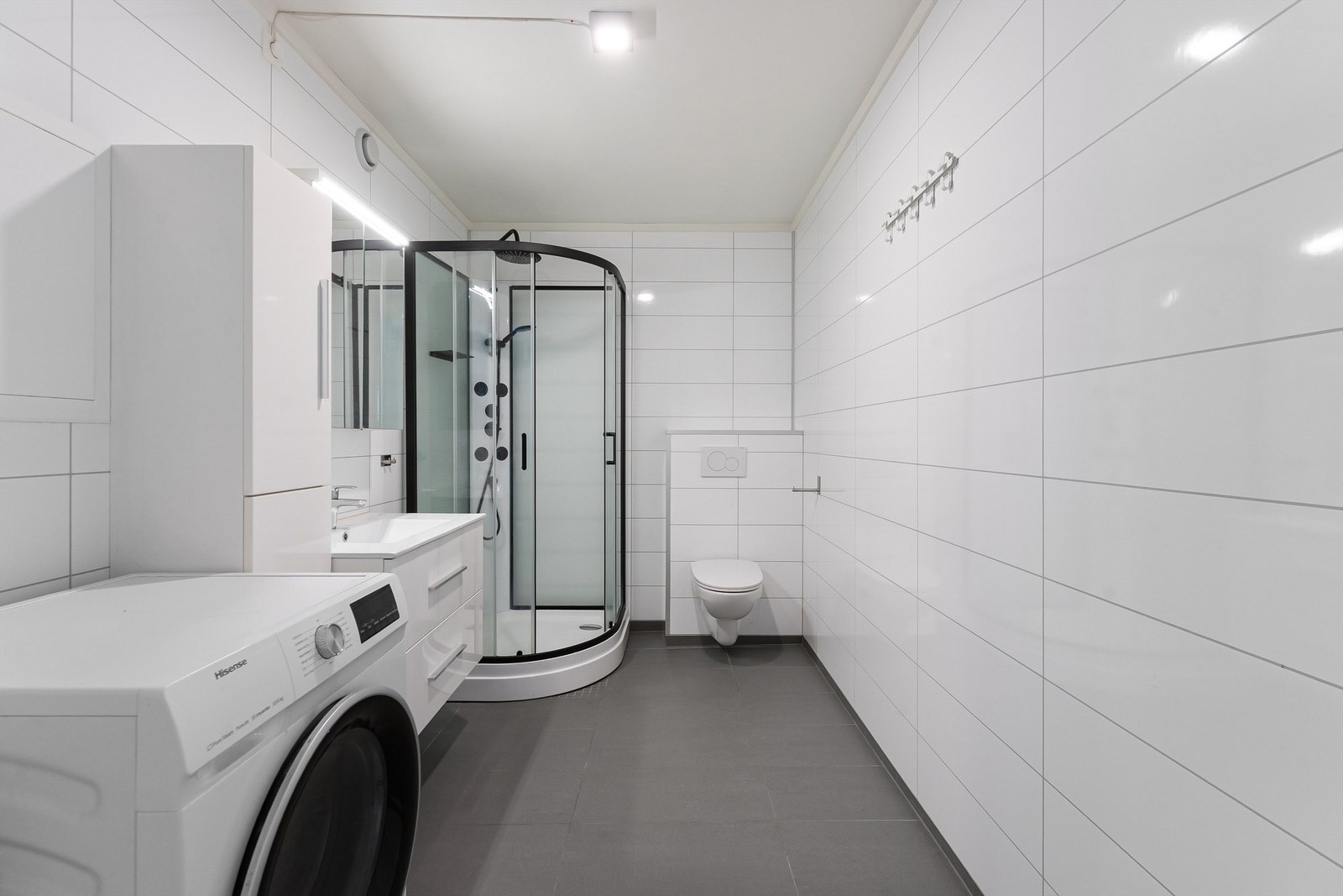 Badet er holdt i nøytrale farger med store, hvite veggfliser og mørkere gulvfliser. Galleribilde