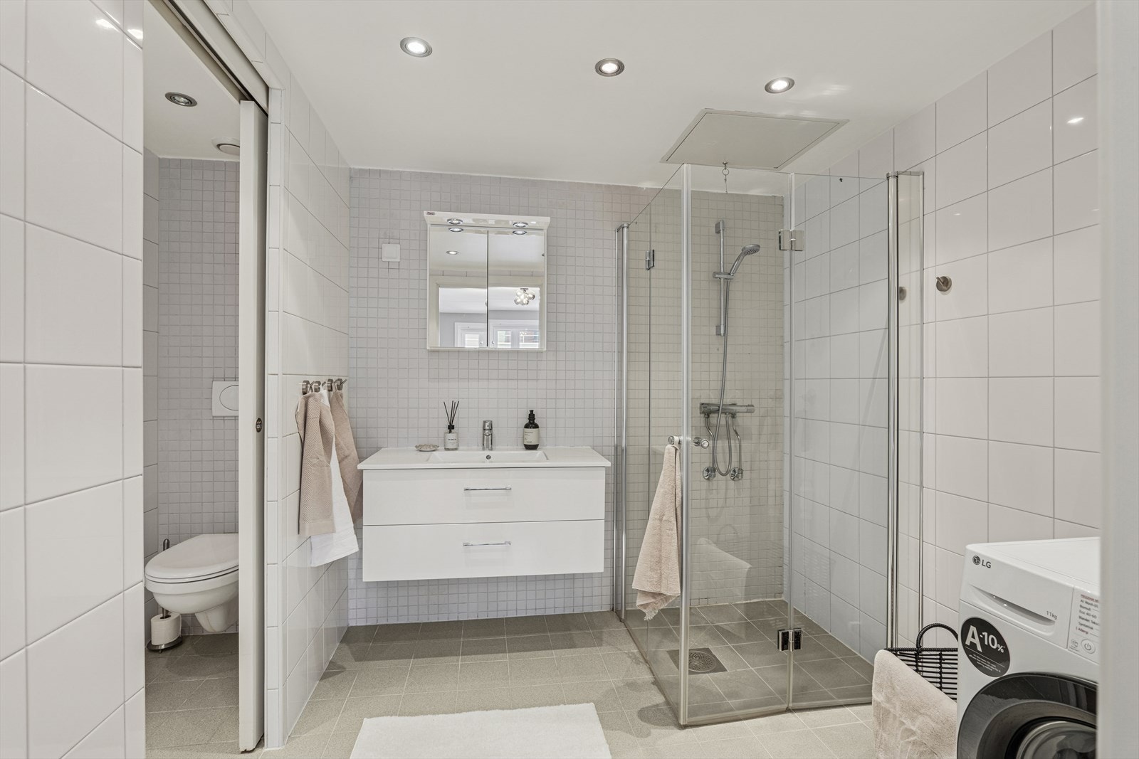 Delikat baderom utstyrt med servant, vegghengt toalett og dusjdører som gir en praktisk og ryddig sone for daglig bruk. Galleribilde