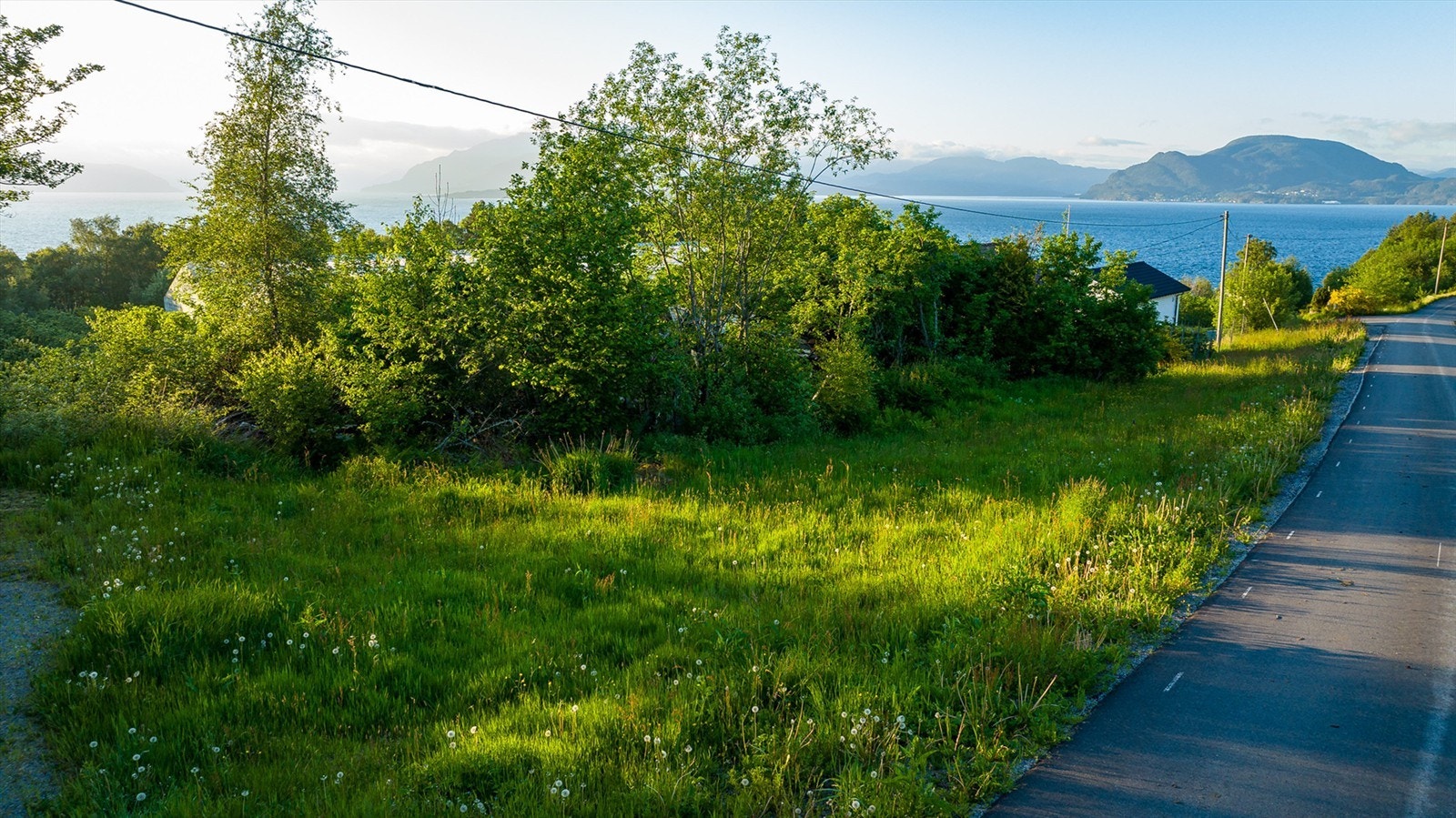 Tomten ligger nær sjøen. Bildet er tatt fra veien ved tomten. Galleribilde