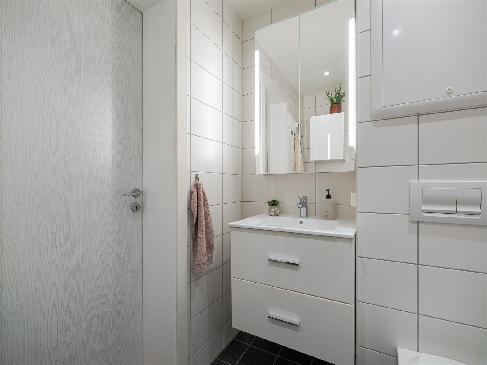 Badet er utstyrt med dusjnisje med glassdører, vegghengt toalett og servant med innredning og speil. Galleribilde