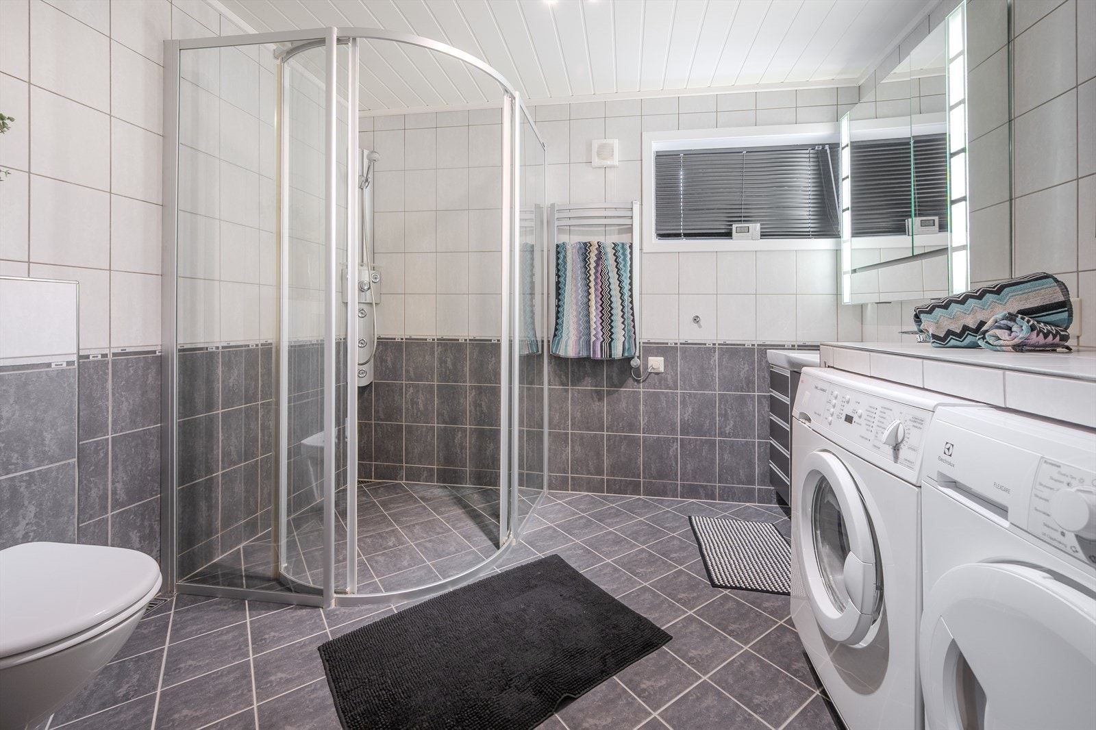 Pent flislagt bad med stort dusjhjørne, vegghengt wc, servant med innredning og opplegg til vaskemaskin/tørketrommel Galleribilde