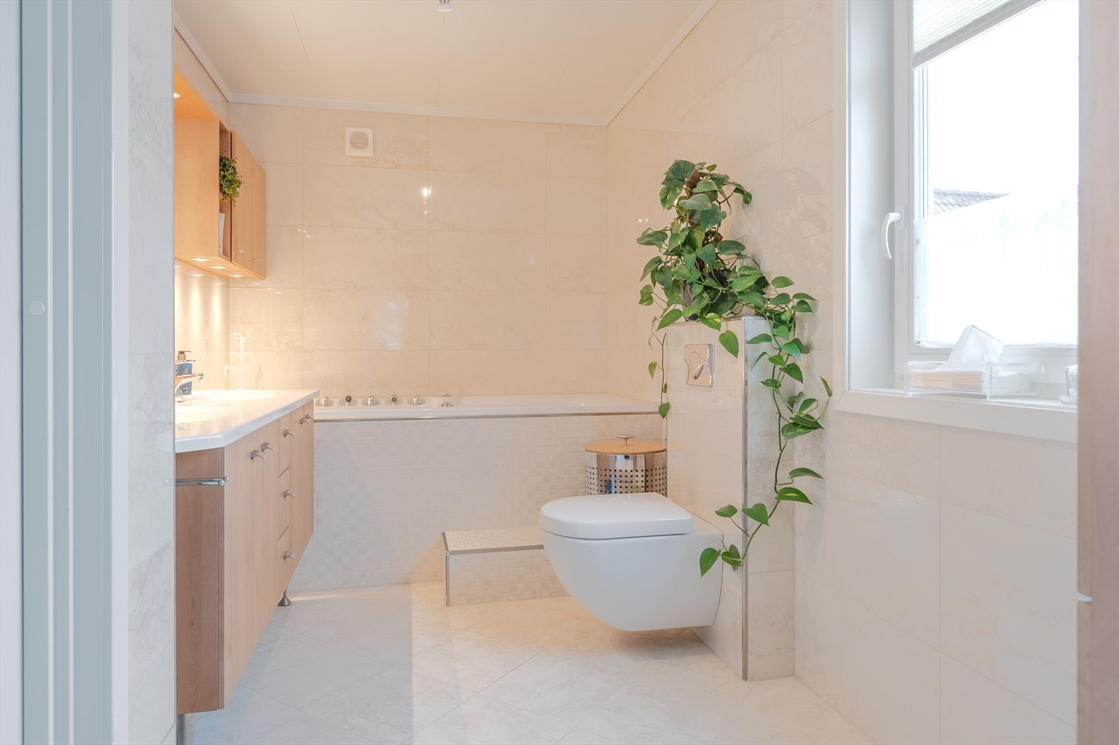 Lekkert flislagt bad romslig badekar, vegghengt wc og heldekkende servant med innredning Galleribilde