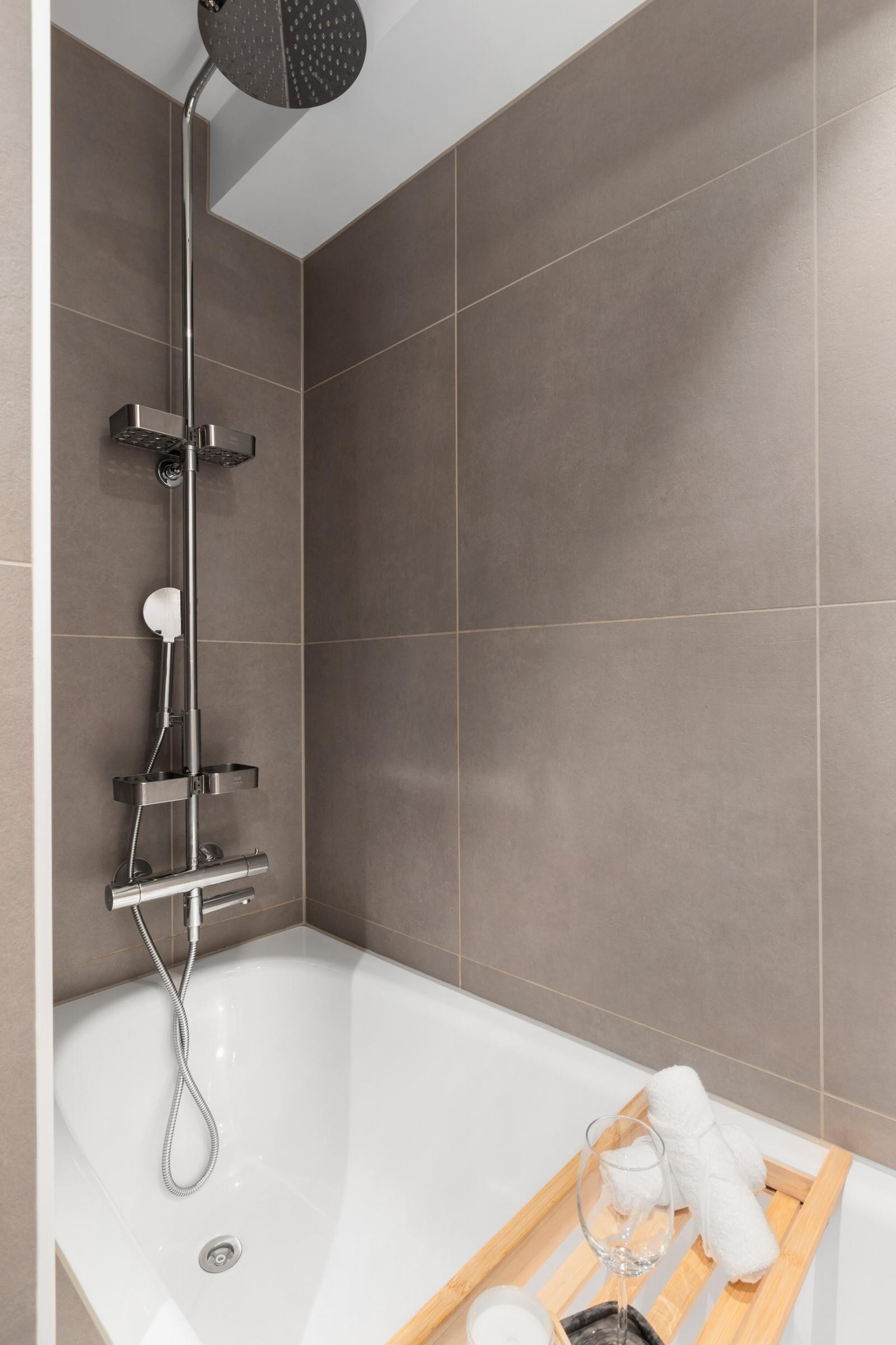 Bad/wc med flislagt badekar, servant med benkeplate og underskap, overskap med speil og et veggklosett. Galleribilde