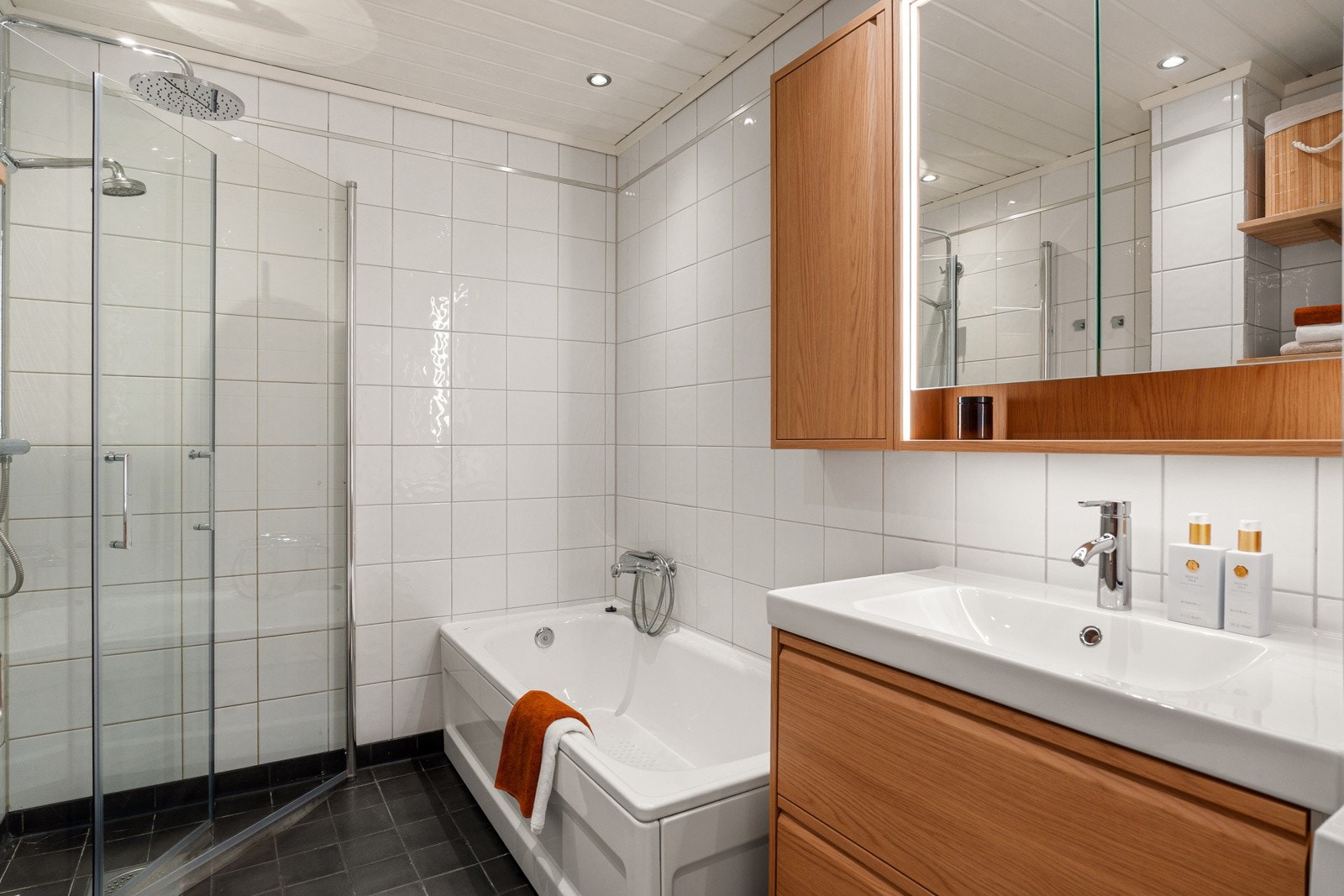 Rommet har en praktisk og funksjonell utforming med servantskap med heldekkende servant, speilskap med belysning, veggmontert toalett, badekar samt dusjhjørne med svingdører og regnfallsdusj. Galleribilde