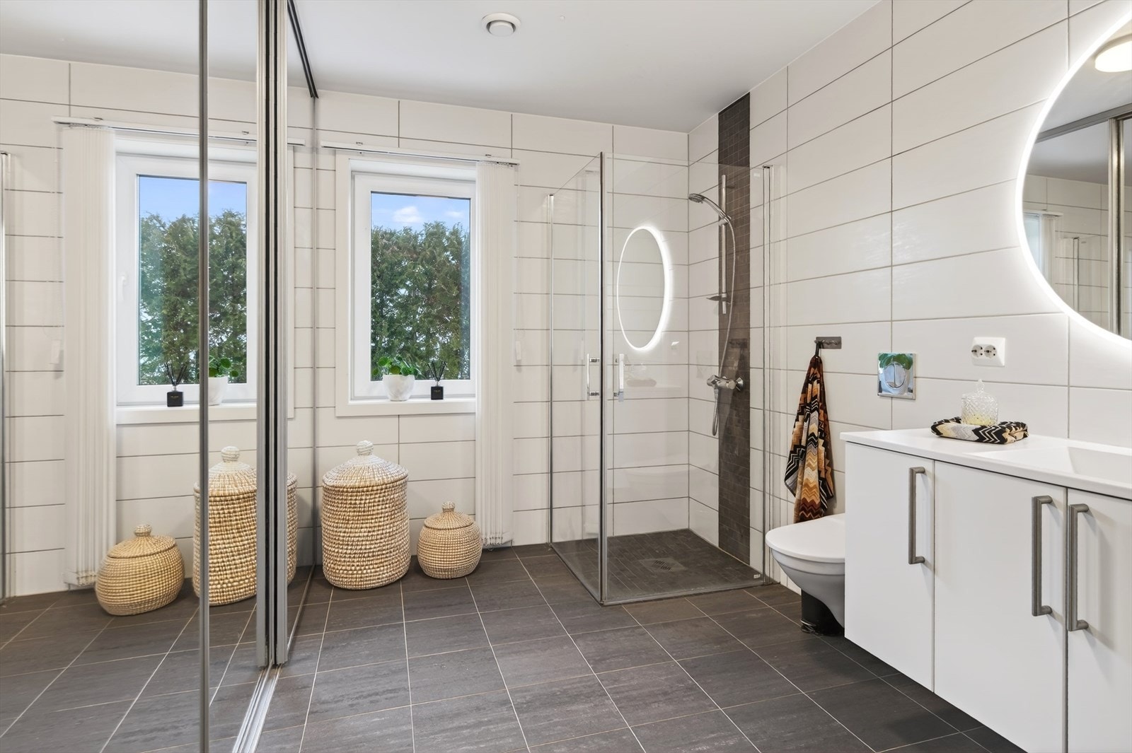 Meget pent flislagt bad med dusjhjørne, vegghengt wc og heldekkende servant med innredning Galleribilde