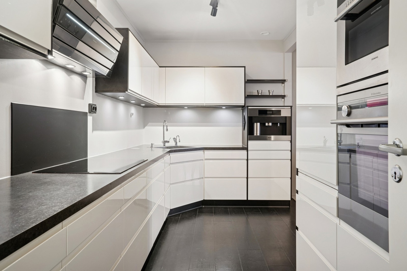 Flott kjøkken med integrerte hvitevarer som, komfyr, induksjonstopp, kjøleskap, oppvaskmaskin og kaffemaskin Galleribilde