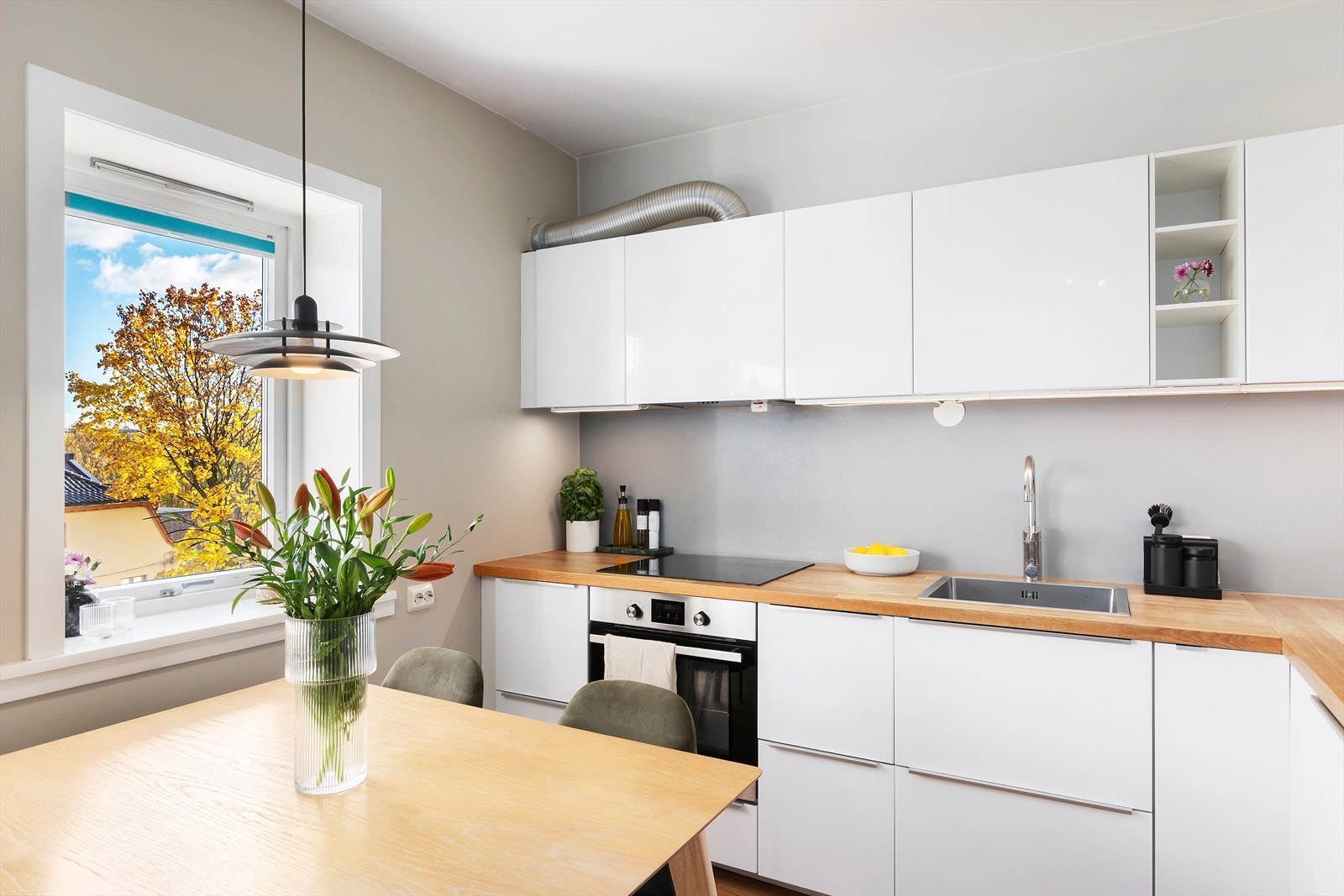 Lys og stilren kjøkkeninnredning fra 2016 bestående av hvite, glatte fronter med benkeplate med nedfelt kum i rustfritt stål Galleribilde