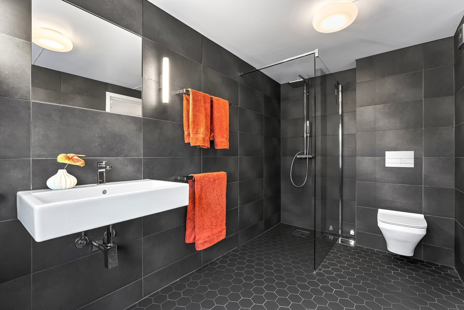 Delikat og romslig flislagt bad med varmekabler i gulv, som sikrer god komfort året rundt. Badet er funksjonelt innredet med servant, vegghengt toalett og dusjløsning på gulv. Galleribilde