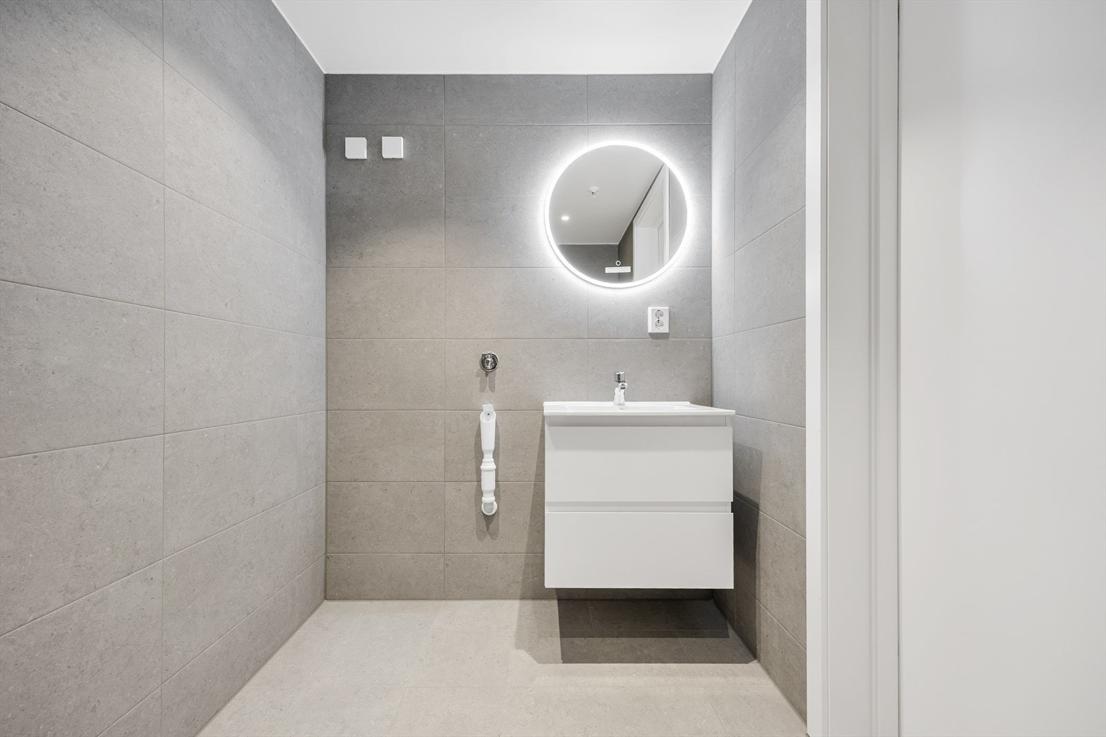 Baderomsinnredning med servant, rundt speil med integrert belysning og opplegg for vaskemaskin. Galleribilde