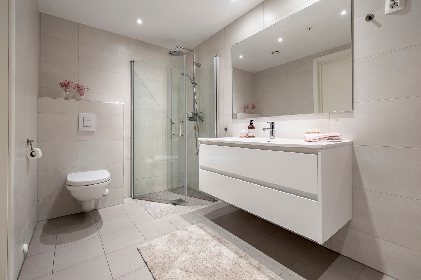 Badet er innredet med servantinnredning, speil på vegg over servant, vegghengt toalett og dusjvegger/hjørne. Galleribilde