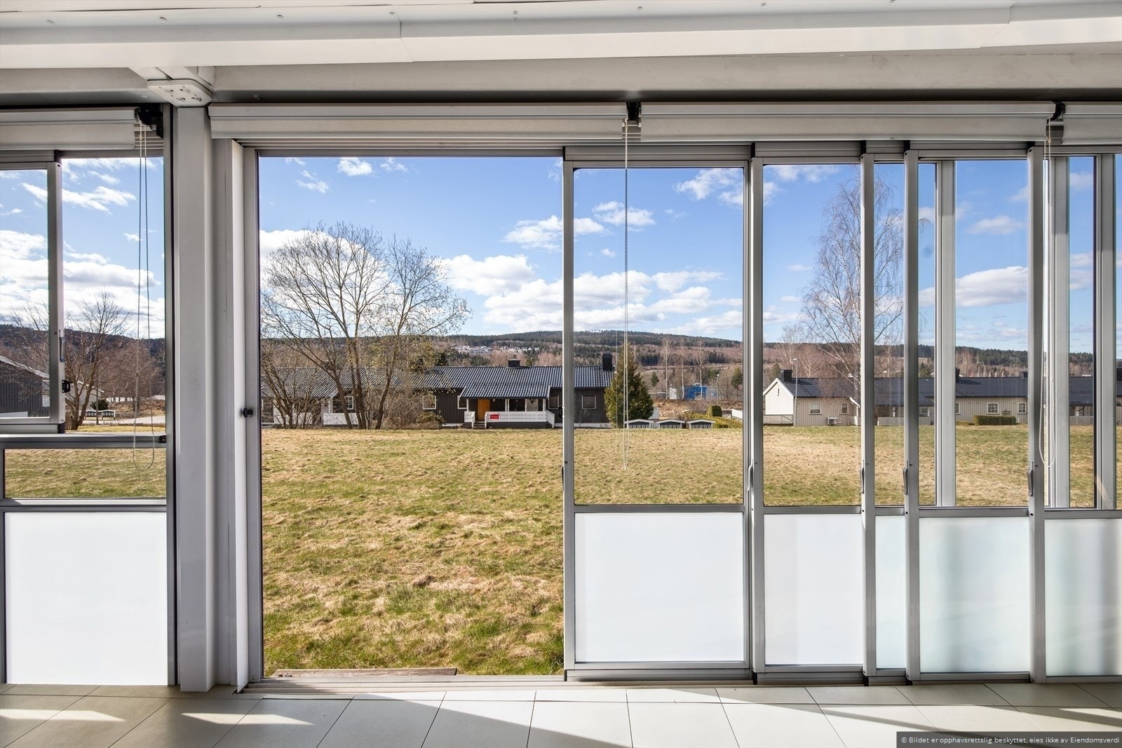 Stor innglasset terrasse på bakkeplan med gode solforhold og utsikt mot grøntområde. Galleribilde