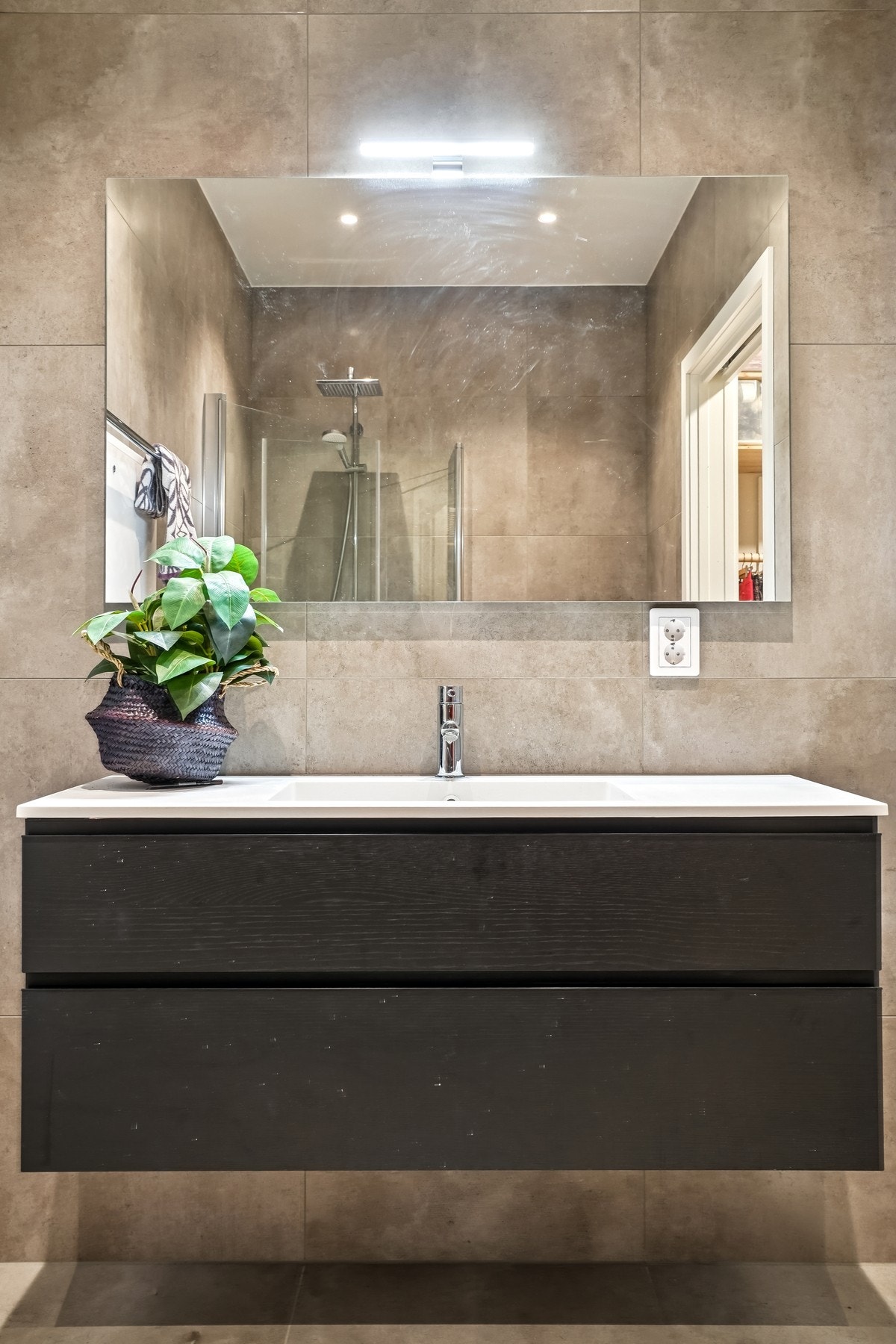 Baderomsinnredning med mørke skuffefronter og hvit helstøpt servant. Speil med belysning over. Galleribilde