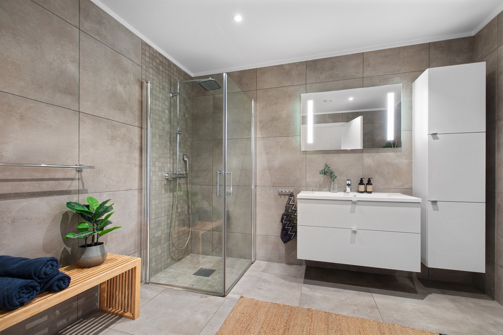 Badet er innredet med dusjnisje med innfellbare glassdører, vegghengt toalett, servantinnredning med speil og belysning samt praktisk høyskap. Galleribilde