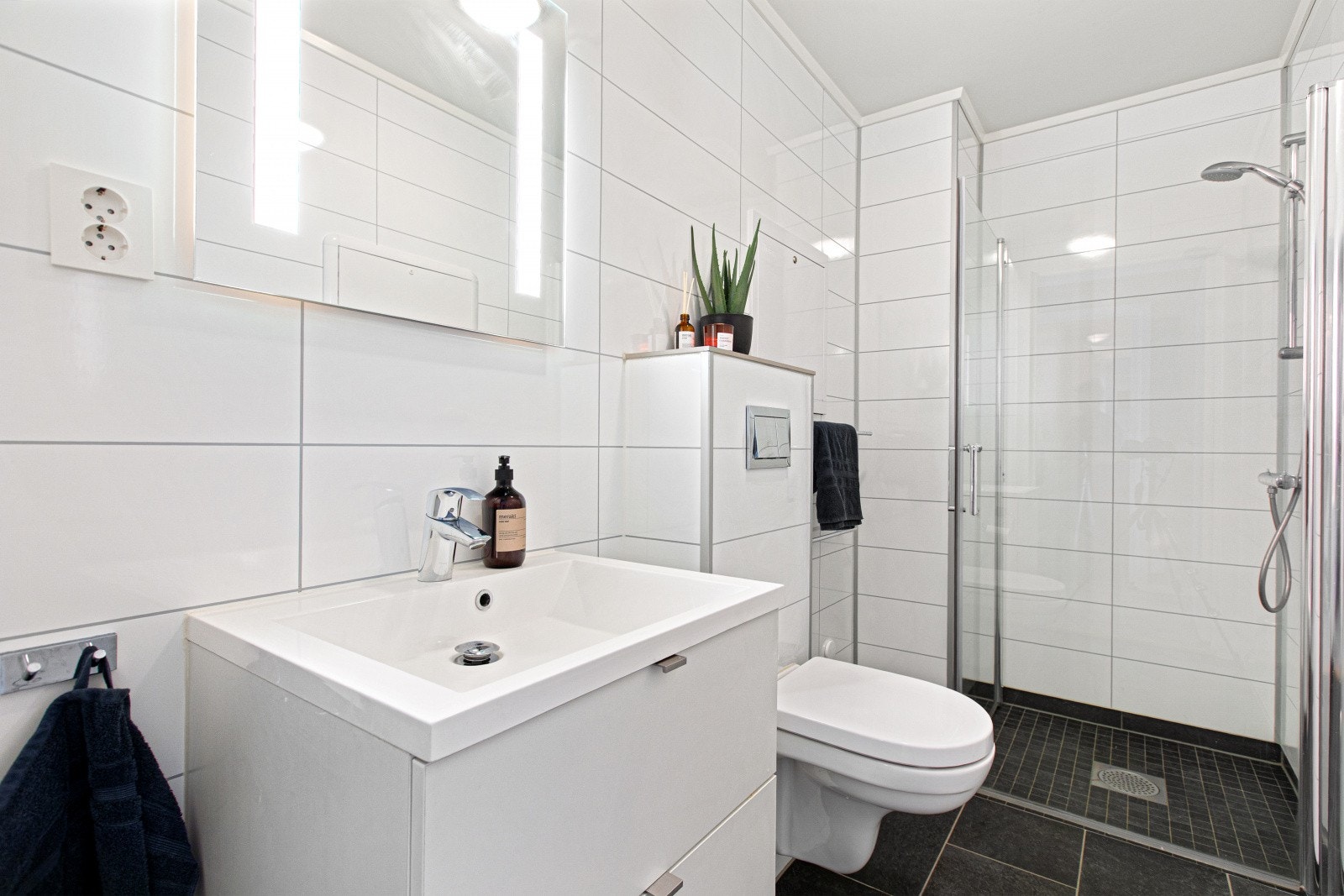 Det første badet er pent flislagt og har et tidløst uttrykk. Badet er innredet med dusjnisje med glassdører, vegghengt toalett og servantinnredning. I tillegg er det varmekabler i gulv og downlights i himlingen. Galleribilde