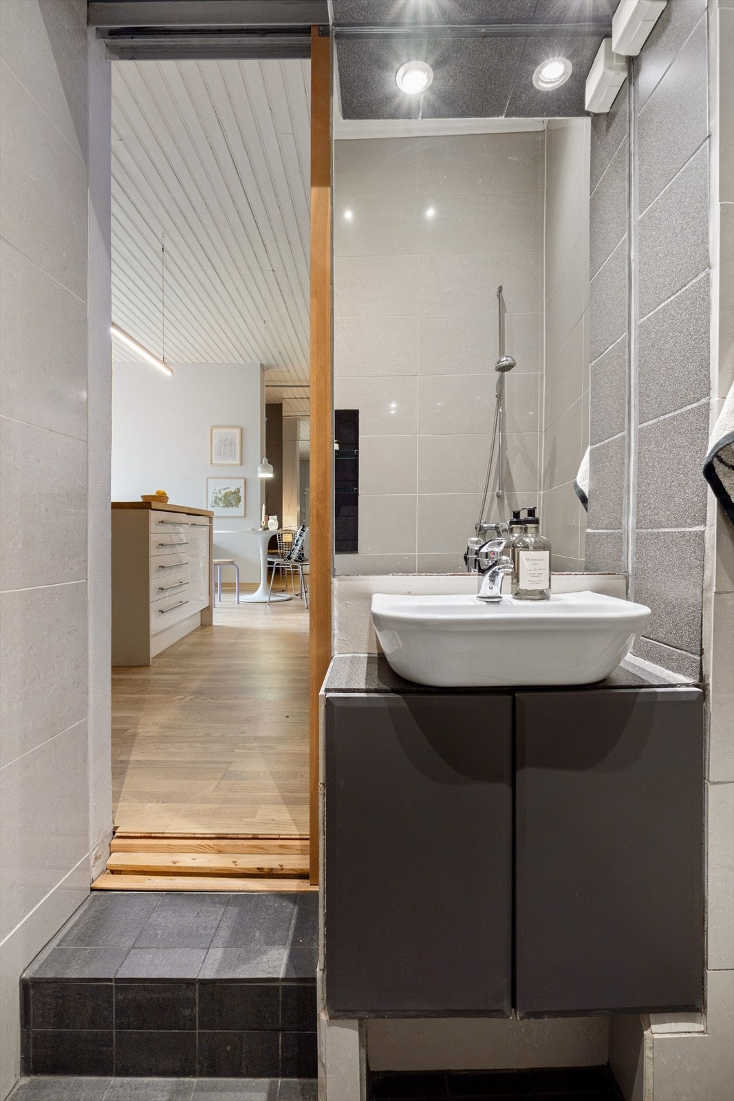 Baderommet er innredet med en servant, overhengende speil og belysning. Dusjen er plassert i hjørnet og har dusjarmatur samt dusjvegger. Videre er det montert et vegghengt toalett. Mekanisk avtrekk. Galleribilde