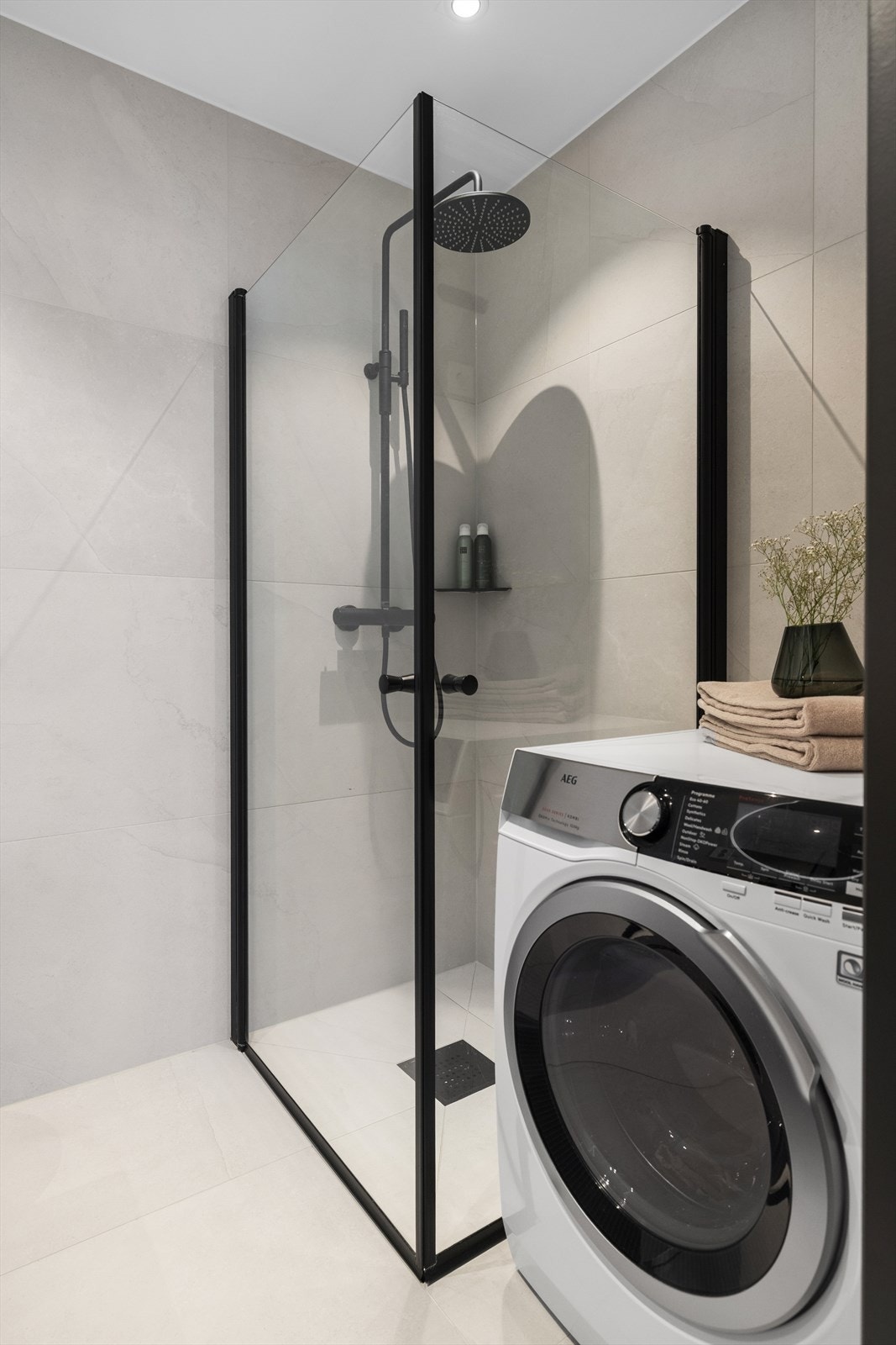 Dusjhjørne med skjermvegger i glass med sorte detaljer i same stil som dusjarmaturet. Galleribilde