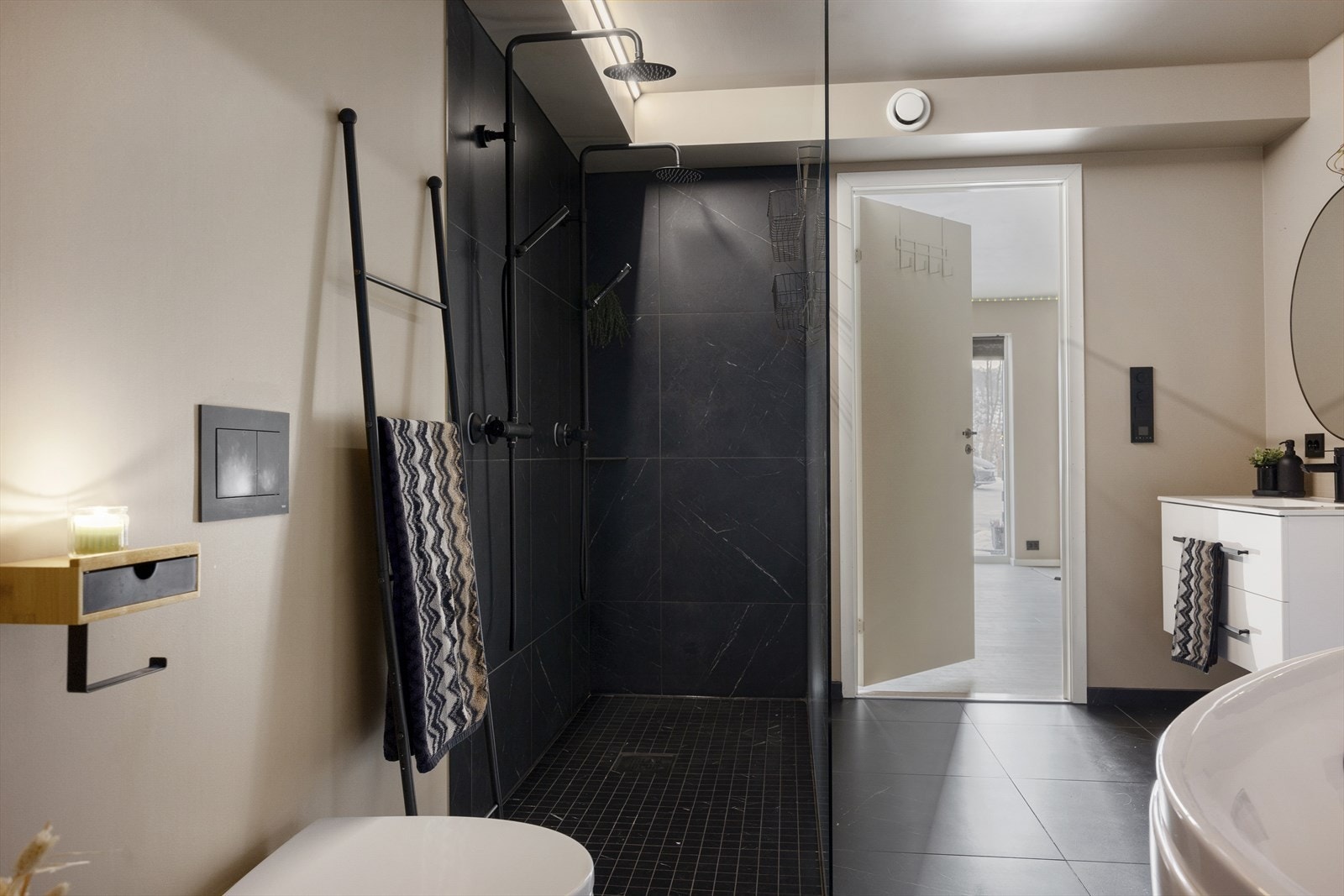 Lekkert bad med fliser på gulvet, lune nyanser på veggene og moderne innredning. Det er utstyrt med romslig baderomsinnredning, vegghengt toalett, badekar, dobbel dusj og nedfelt servant. Galleribilde