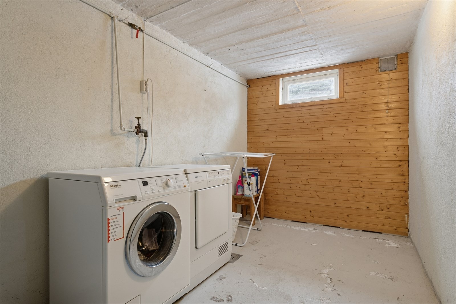 Praktisk vaskekjeller med malt betonggulv og opplegg for vaskemaskin. Galleribilde