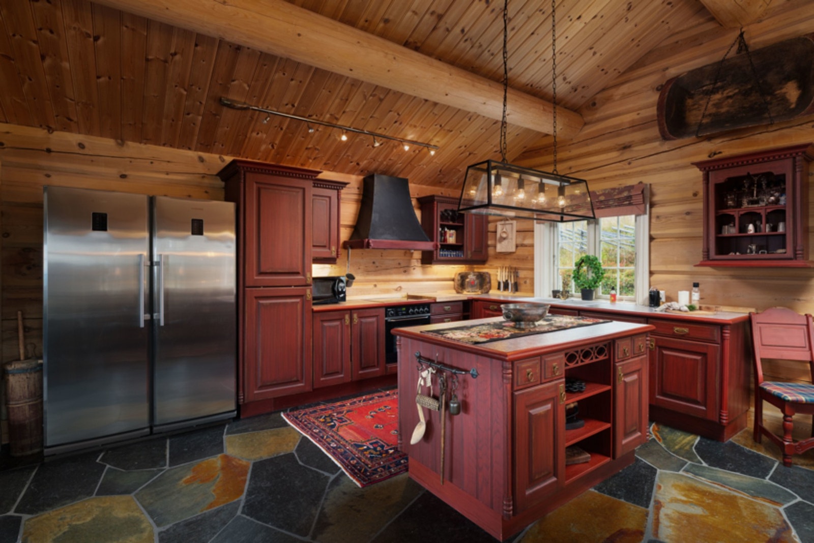 Tradisjonell kjøkkeninnredning med aldringsmalte fronter, malt i en dyp farge i stil med hytten, heltre benkeplater, integrerte hvitevarer bortsett fra kjøl/fryseskap for et sømløst resultat. Galleribilde