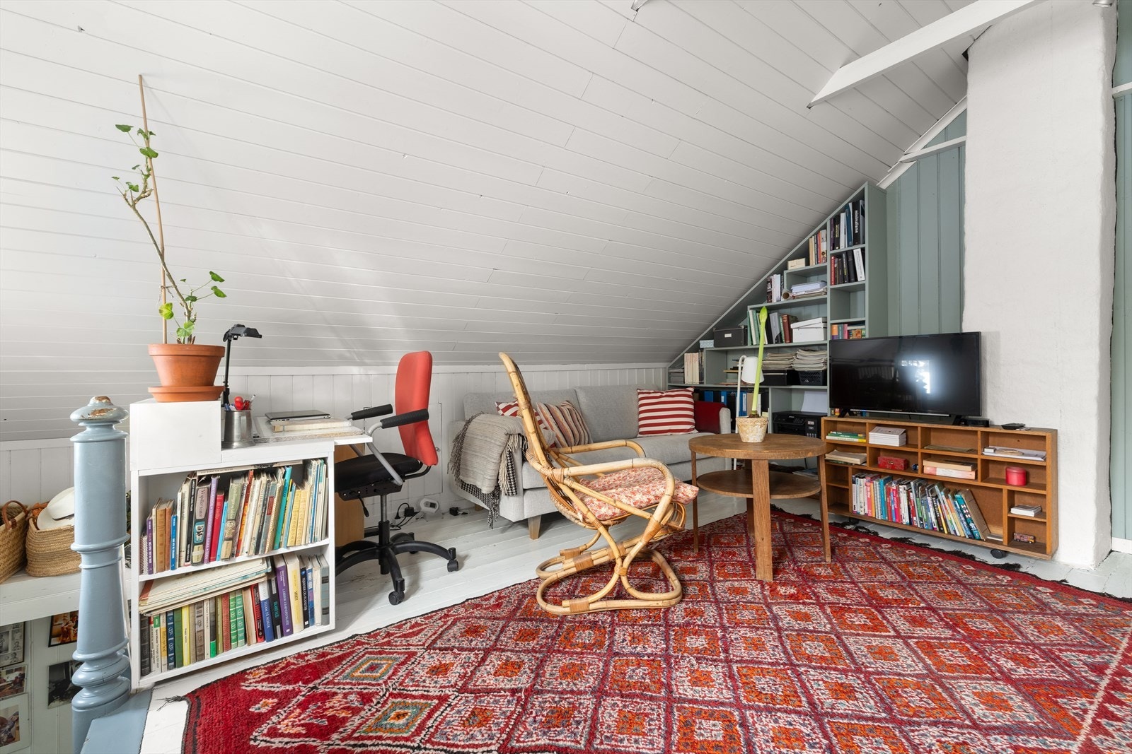 Skråtak og panelvegger gir rommet en unik karakter, mens innebygde hyller tilbyr praktisk oppbevaring. Galleribilde