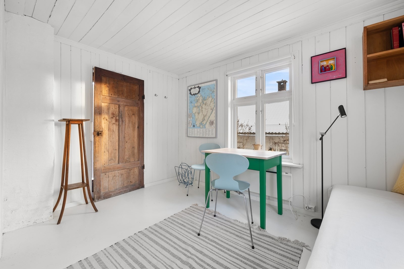 Hvite panelvegger og tregulv skaper et lyst og innbydende rom med naturlig lysinnslipp. Galleribilde