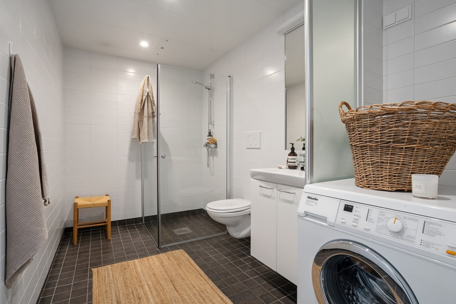 Flislagt bad med tidsriktige overflater bestående av lyse veggfliser og mørke gulvfliser. Badet er innredet med servant med skap med glatte fronter, samt speil over servant. Galleribilde